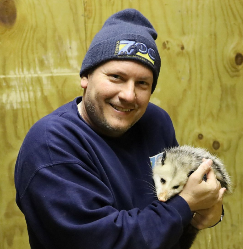 smiling male in navy blue winter cap and sweater holding opossum