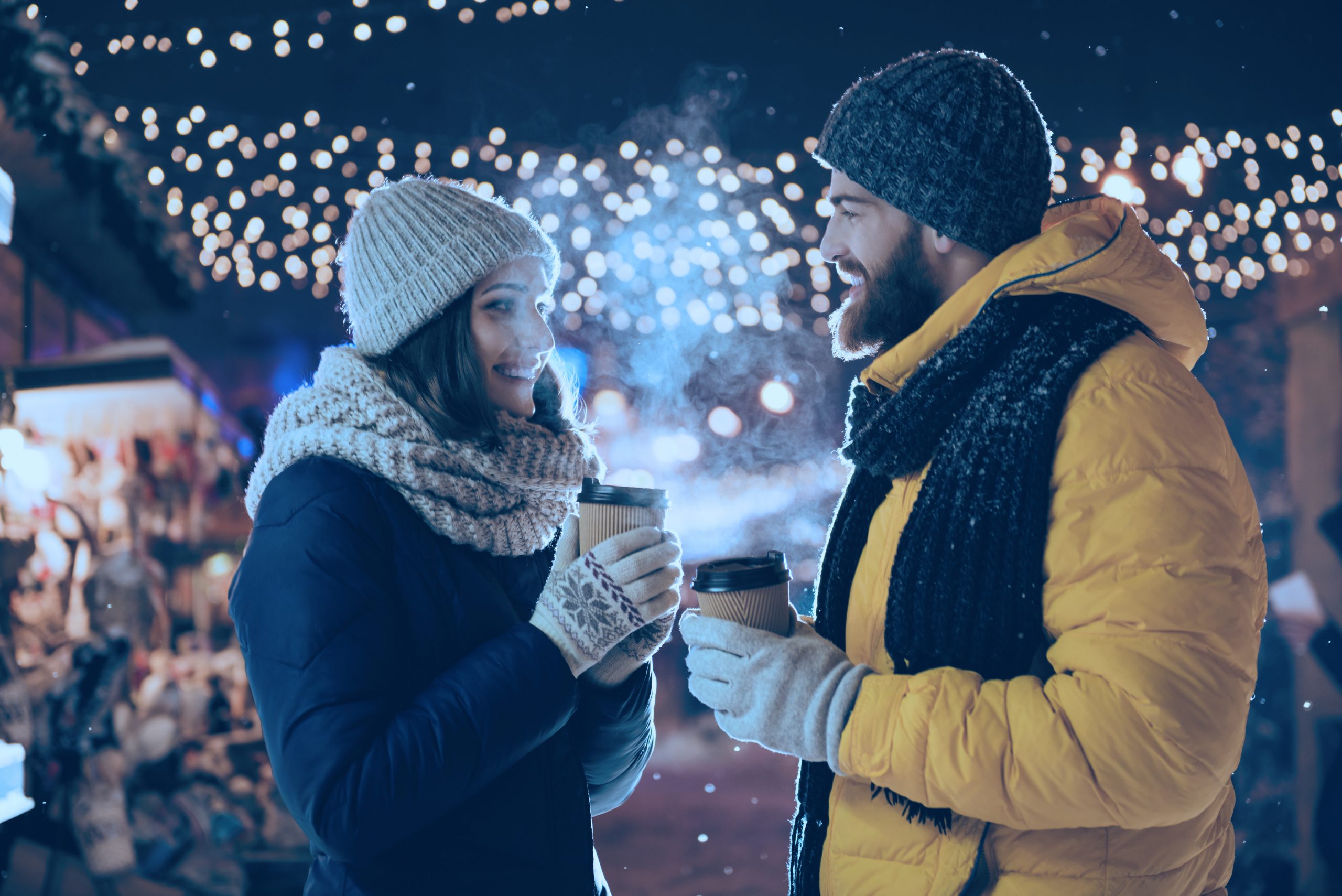 Photo of two people talking couple husband guy wife lady drink hot beverage, spend x-mas eve magic land newyear shopping market buying gifts wear jackets outside